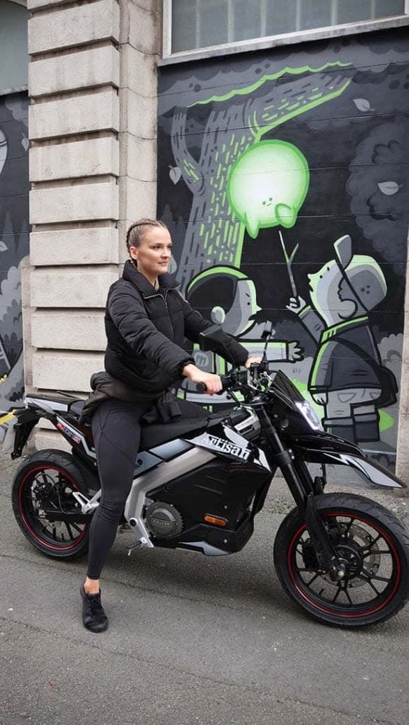 Blonde lady sitting on motorbike in front of street graffiti