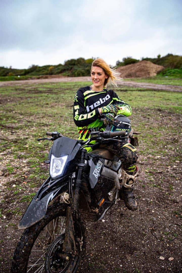 Blonde woman in bike gear sitting on electric bike in a muddy field