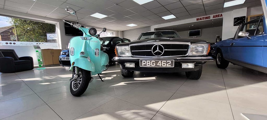 Green electric moped next to a Mercedes SL inside Checkpoint showroom