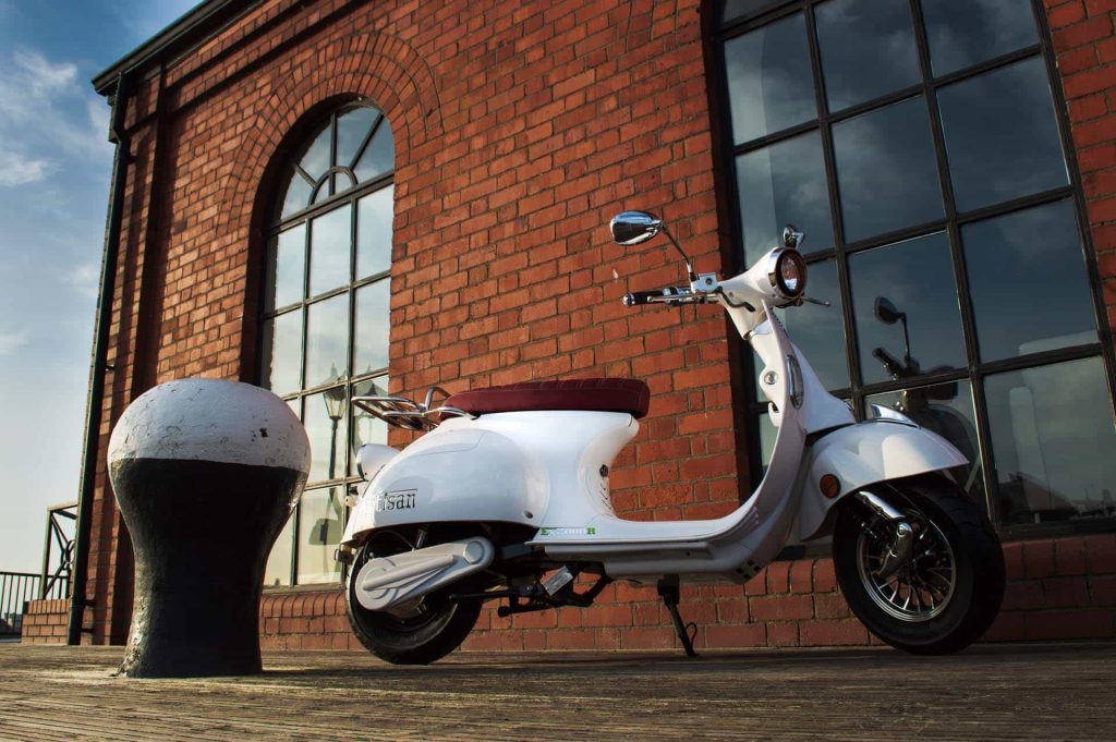 White electric road legal scooter in front of brick building by shipping bollard