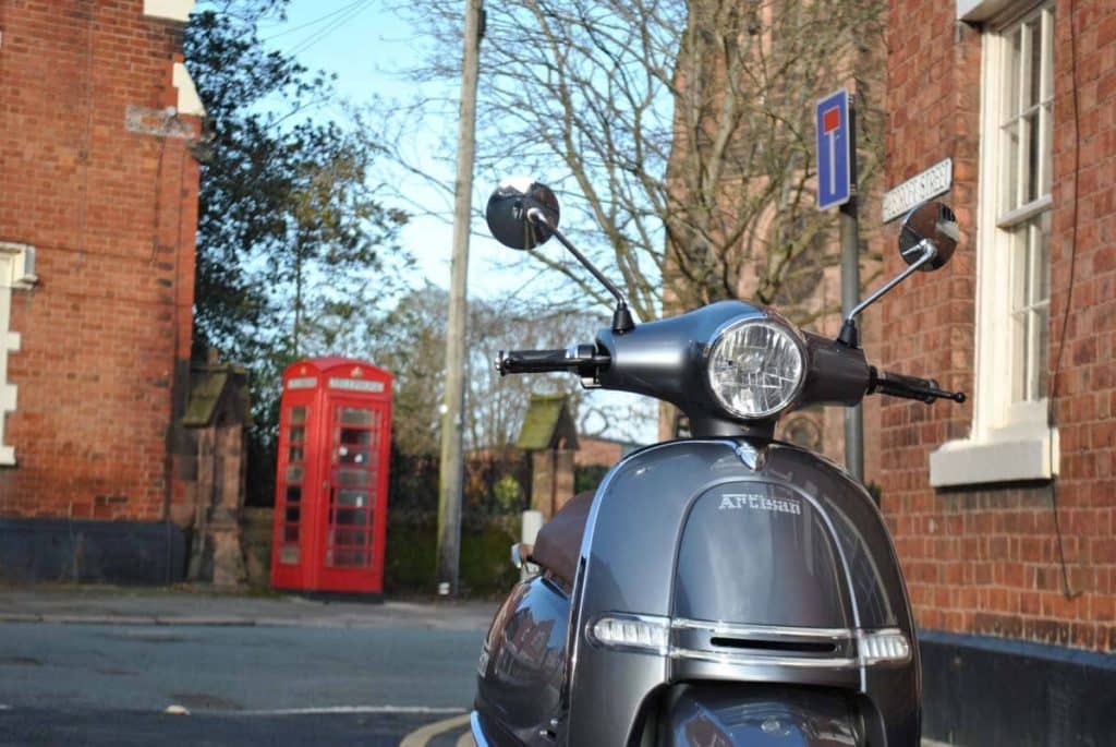 Grey electric Artisan moped on street with old fashioned red public telephone box